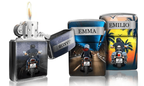 Drei Zippo-Feuerzeuge mit individuellen Designs: eines brennt und zeigt eine nächtliche Autobahnszene, ein anderes zeigt einen Fahrer mit „EMMA“ und das dritte einen Sonnenuntergang mit „EMILIO“.