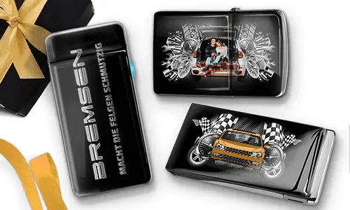 Elegante schwarze Feuerzeuge mit Auto-Designs. Eines zeigt eine Familie in einem Auto, ein anderes ein blaues Auto mit karierten Flaggen. Daneben liegt eine Geschenkbox mit goldener Schleife.