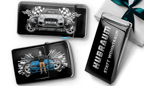 Geschenkset mit Auto-Themen-Metallbehältern, die Bilder eines grünen Sportwagens, karierten Flaggen und Motor-Motiven zeigen. Enthält ein Zigarettenetui mit der Aufschrift „Hubraum Statt Wohntraum“.