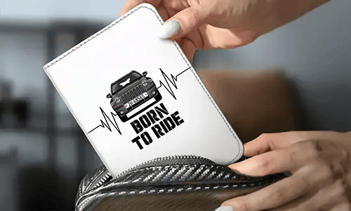 Persona tiene un portafoglio bianco con auto nera e design con battito cardiaco, scritta BORN TO RIDE, zaino in fibra di carbonio sullo sfondo