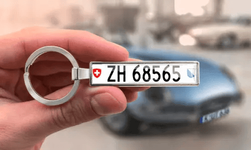 Porte-clés avec plaque d’immatriculation personnalisée, tenu en main avec une voiture en arrière-plan