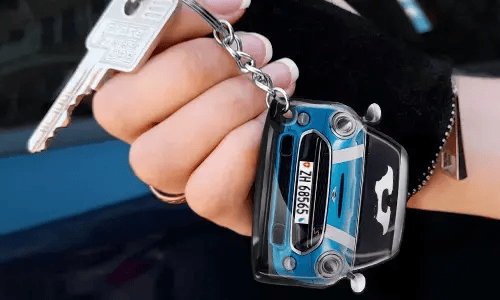 Hand holding a keychain shaped like a blue car with detailed front design