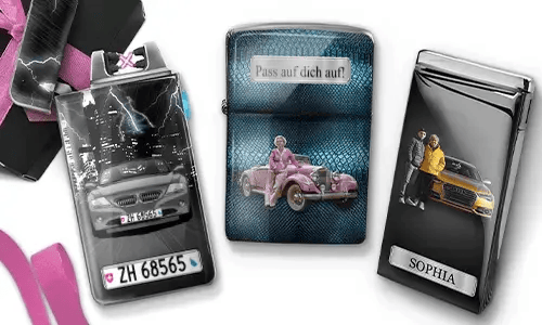 Three metal lighters featuring personalized designs. The left lighter shows a city skyline and a couple beside a car with 'BESTE OMA DER WELT'. The middle lighter depicts a pink vintage car with 'HAB DICH LIEB OMA' above. The right lighter displays a blue car and a license plate. Pink ribbons add a gift-like context.
