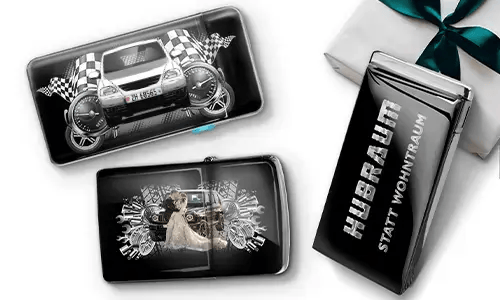 Three black wallets with car-themed designs and checkered flags, set against a white background. One shows a car with wheels, another features a couple, and one has 