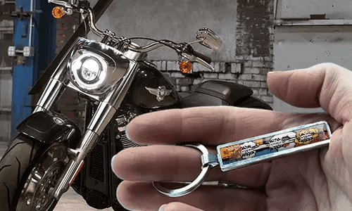 Porte-clés en métal style comic avec illustration de moto, tenu à la main près de la moto