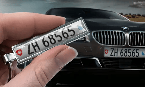 Llavero de matrícula en estilo cómic, sostenido en una mano frente a un coche con matrículas a juego