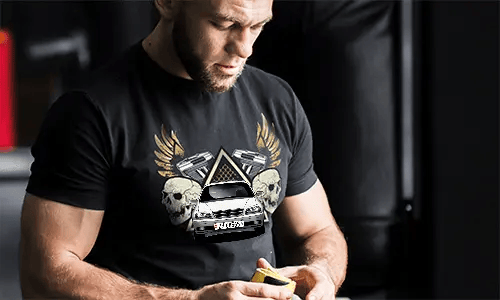 Black T-shirt with graphic of car, skulls, pistols, golden wings, and starry triangle background